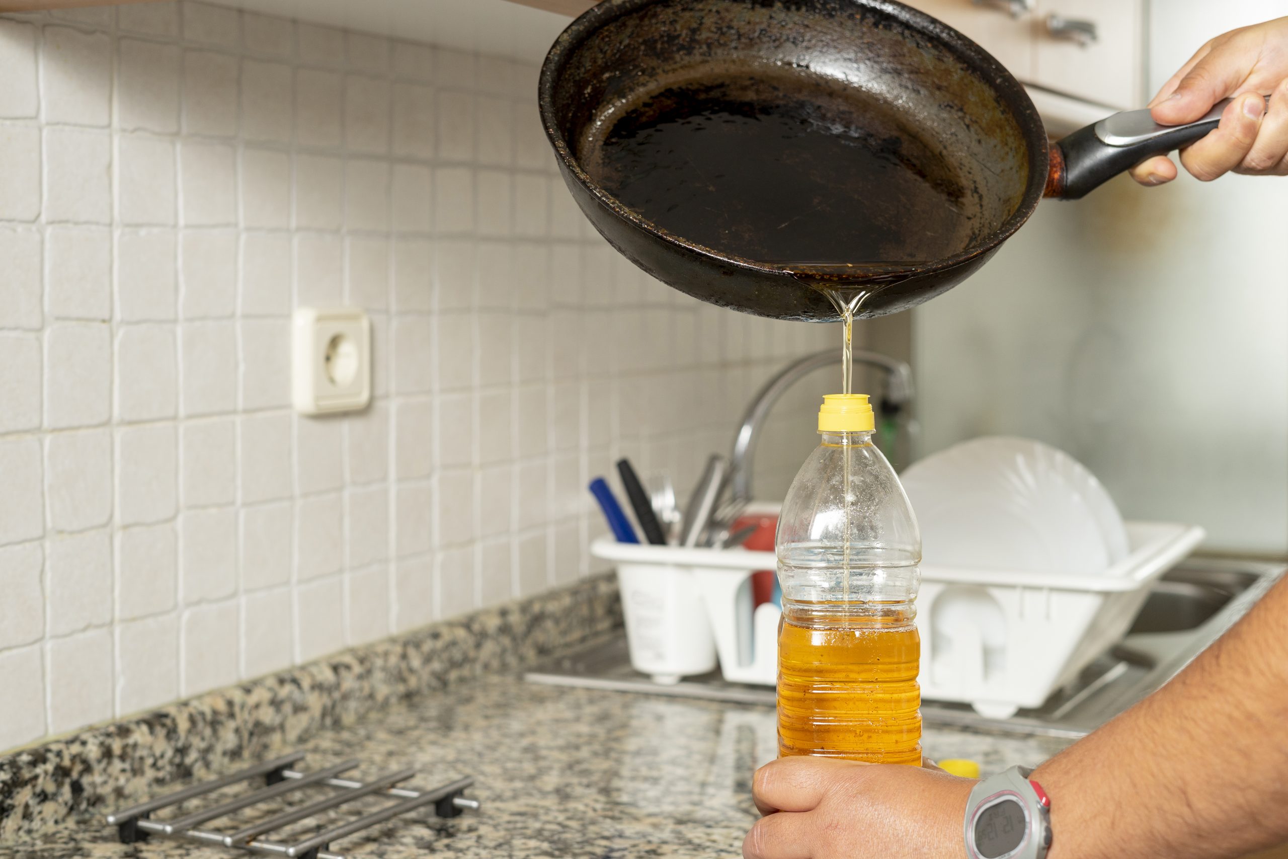 Man placing recycled edible oil from a frying pan into a plastic bottle in his home kitchen. Recycle at home concept. High quality photo